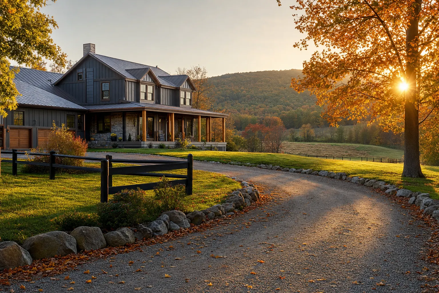 A country house with a wraparound porch sits beside a winding driveway and a large tree at sunset.